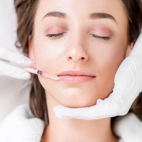 Woman receiving a botox injection in the lips zone lying on the medical couch