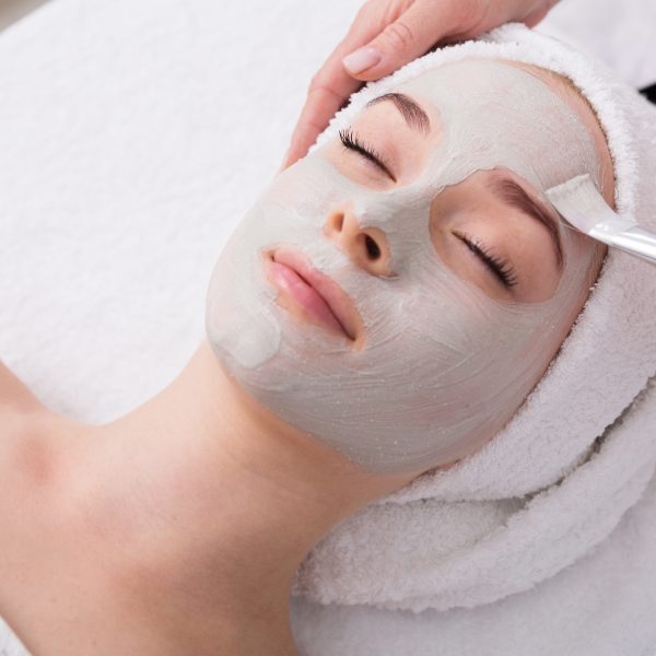 Face peeling mask, spa beauty treatment, skincare. Woman getting facial care by beautician at spa salon, side view, close-up