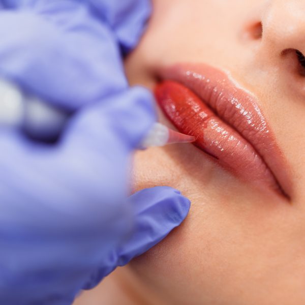 Young woman having permanent makeup on lips in beautician salon. Close up